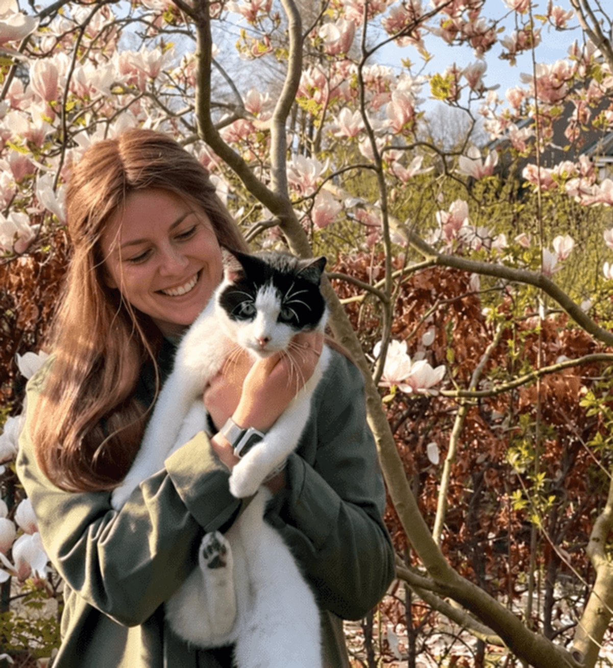 Vrouw met lang bruin haar en een kat in een bloeiende tuin